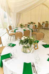Close up of wine glasses, silver tableware and green napkins on round tables covered with white tablecloth.