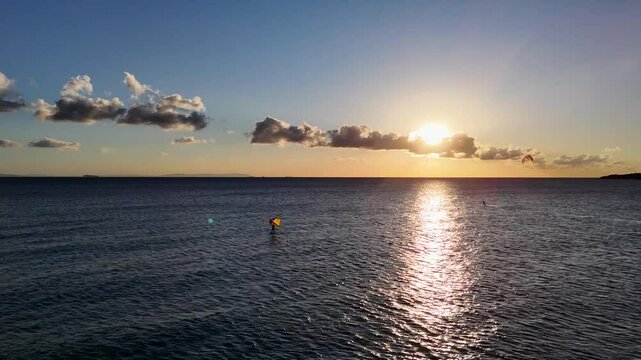 Der Blick zeigt die untergehende Sonne, den Ozean und die Silhouette von Afrika am Horizont. Sanfte Wellen brechen am Ufer, w&auml;hrend der Himmel in warmen Farben leuchtet.

