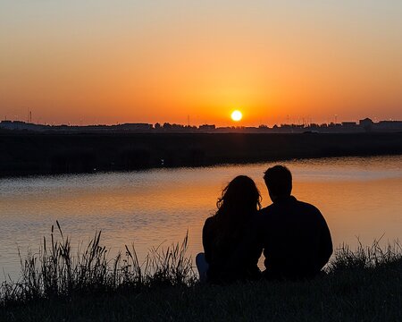 Silhouette of couple watching sunset by lake.