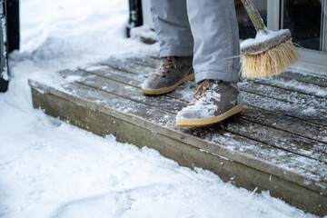 Close-up of a person using a broom to clear snow from a winter shoes. 
