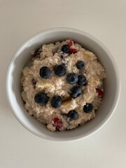 A top view of a round bowl filled with oatmeal topped with strawberry pieces and blueberries, representing a healthy and nutritious meal for those mindful of their well-being.