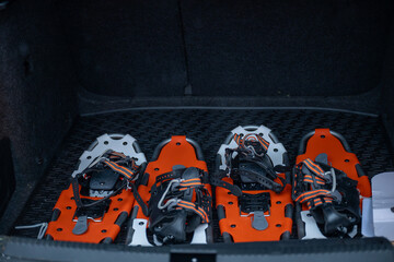 Four snowshoes with orange and white details placed in a car trunk, black interior. Concept of winter sports and outdoor equipment