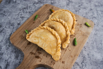 Kue Pastel or Jalangkote, Indonesian traditional snack filled with carrot and potatoes served On Wooden Cutting Board With Fresh Green Chilis