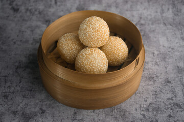 Traditional Sesame Ball Pastries in Bamboo Steamer on Textured Background