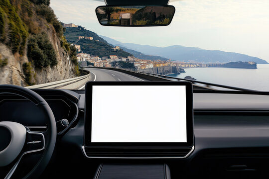 A white blank mock-up touchscreen in a modern car with a minimalist interior driving on the road with a coast in the background