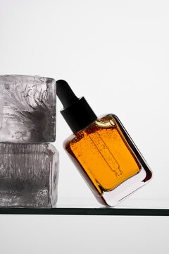Vitamin C Serum in Glass Bottle with Ice Block on Glass Surface