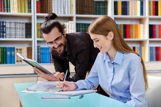 Teenage student girl studying with male teacher inside classroom library