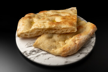 Slices of flatbread focaccia on white marble plate on black background
