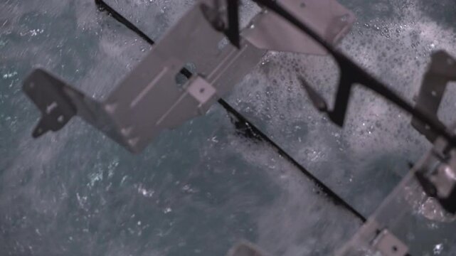 Close up view of dipping hanged metal pieces in the electropaint tank for the cataphoresis or paint process on the automated conveyor in a factory.