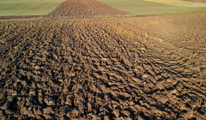 Fototapeta premium Aerial view of freshly plowed agricultural field with textured soil patterns and green patches in the background.