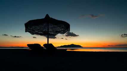 The beginning of the day at the Red Sea. Dark silhouettes of a chaise lounge and an umbrella can be...