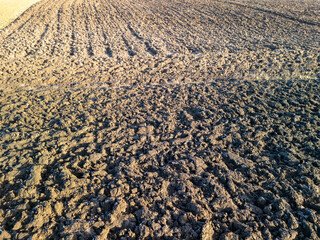 Dry, cracked soil in a plowed field under sunlight, showcasing agricultural patterns and rich earth texture.