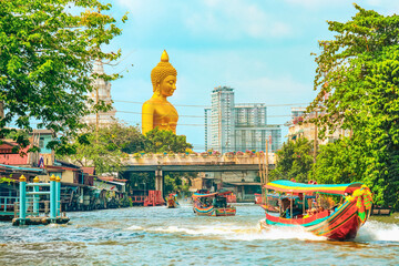 View of big  Buddha statue in Bangkok, Thailand (Wat Pak Nam Phasi Charoen) from canal with wooden houses and long tails boats