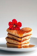 A stack of heart-shaped pancakes topped with syrup and a small red flower