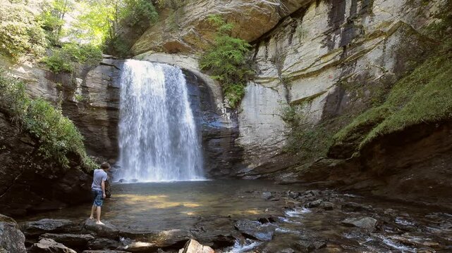 Slow motion shot of teen wading near Looking Glass Falls in forest in North Carolina.