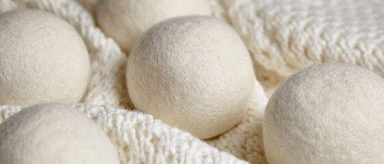 Close-up of white wool dryer balls arranged on a textured, soft knitted blanket, creating a cozy, eco-friendly feel. Ideal for illustrating sustainable home care essentials