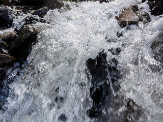 Obraz premium Close-up of a fast-moving mountain river: rushing waters reflecting sunlight and sparkling drops in a stunning natural setting