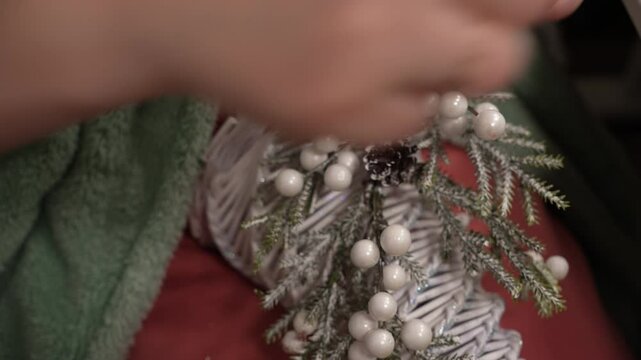 A person skillfully arranges pine, berries, and decorative elements for a winter-themed display. The cozy atmosphere adds a warm touch to the creative process of crafting.