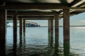Underneath of a concrete bridge with sunlight reflecting on the calm water