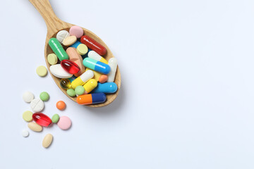 Various pills in wooden spoon on white background