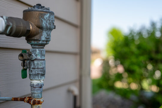 Rusted outdoor water sprinkler backflow preventer on the side of a residential house