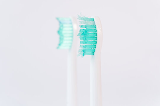 A worn-out ultrasonic toothbrush head, now unusable, stands in the foreground. In the background, a new head with perfectly straight bristles is visible.