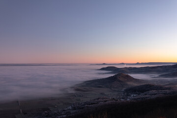 Fototapeta premium Blick vom Breitenstein, Ochsenwang, Schwäbische Alb auf die drei Kaiserberge - Hohenstaufen, Stuifen und Rechberg. Im Vordergrund die Limburg bei Weilheim Teck im Winter zum Sonnenaufgang mit Nebel.