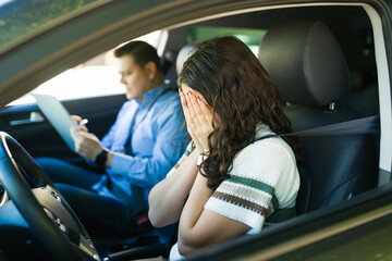 Anxious teen hiding her face after unsuccessful driving test as instructor records errors during road lesson