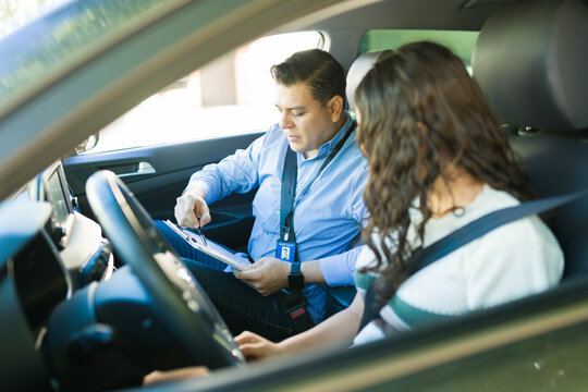 Male driving instructor giving driving test instructions to a teenage student inside a car