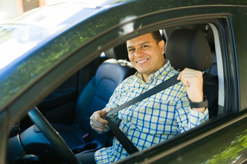 Happy latin man fastening his seat belt while driving a car, road safety concept
