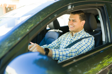 Happy hispanic man wearing a seatbelt while driving to work in his car