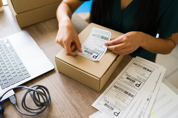 Closeup of a female business owner preparing a shipment, affixing a priority mail label to a...