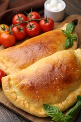 Tasty vegetarian calzones with basil, tomatoes and mozzarella cheese on wooden table, closeup