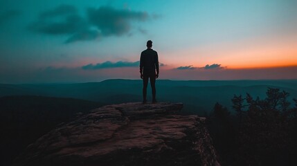 Obraz premium Man silhouetted on mountaintop at sunset.