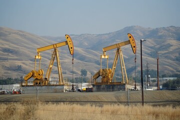 Two oil derricks pump near hills.