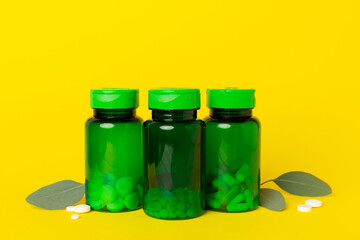 Bottles with pills and green leaves on color background