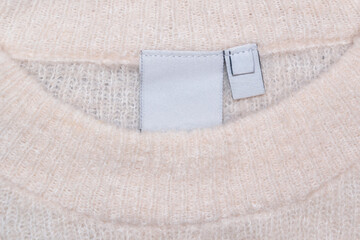 Close-up of a beige wool sweater with a blank inner label.The soft, warm knit fabric complements the empty tag.