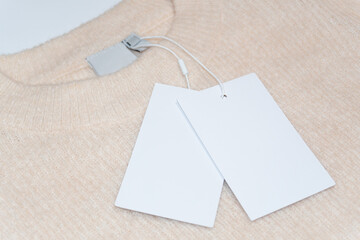 A close-up of a beige wool sweater with an empty label on the inside of the neckline and clean white tags attached to the garment.