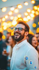 Obraz premium A joyful man with glasses smiles brightly at a lively outdoor gathering illuminated by warm string lights.