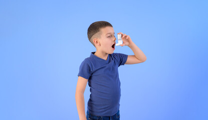 Portrait of adorable boy inhaling through asthma pump while standing against isolated blue background