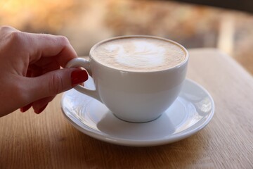 Woman with cup of aromatic coffee at wooden table in cafe, closeup