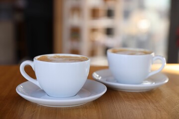 Cups of aromatic coffee on wooden table in cafe, closeup