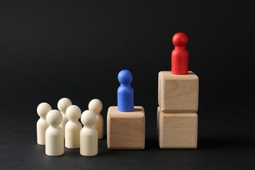 Competition concept. Human figures on wooden cubes and other ones behind against black background
