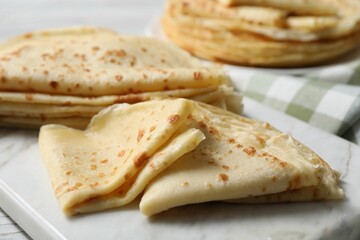 Many tasty crepes on white wooden table, closeup