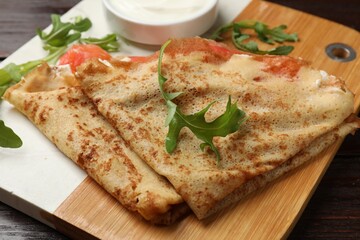 Delicious crepes with salmon, cream cheese and arugula on wooden table, closeup