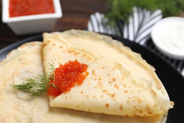 Tasty crepes with red caviar and dill on table, closeup