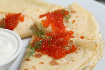 Tasty crepes with red caviar, dill and sauce on plate, closeup