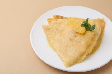 Plate with tasty crepes Suzette on beige table, closeup. Space for text