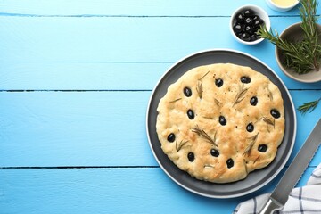 Delicious focaccia bread with olives and rosemary on light blue wooden table, flat lay. Space for text