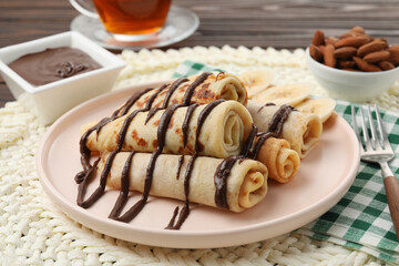 Delicious crepes with chocolate sauce and banana served on table, closeup